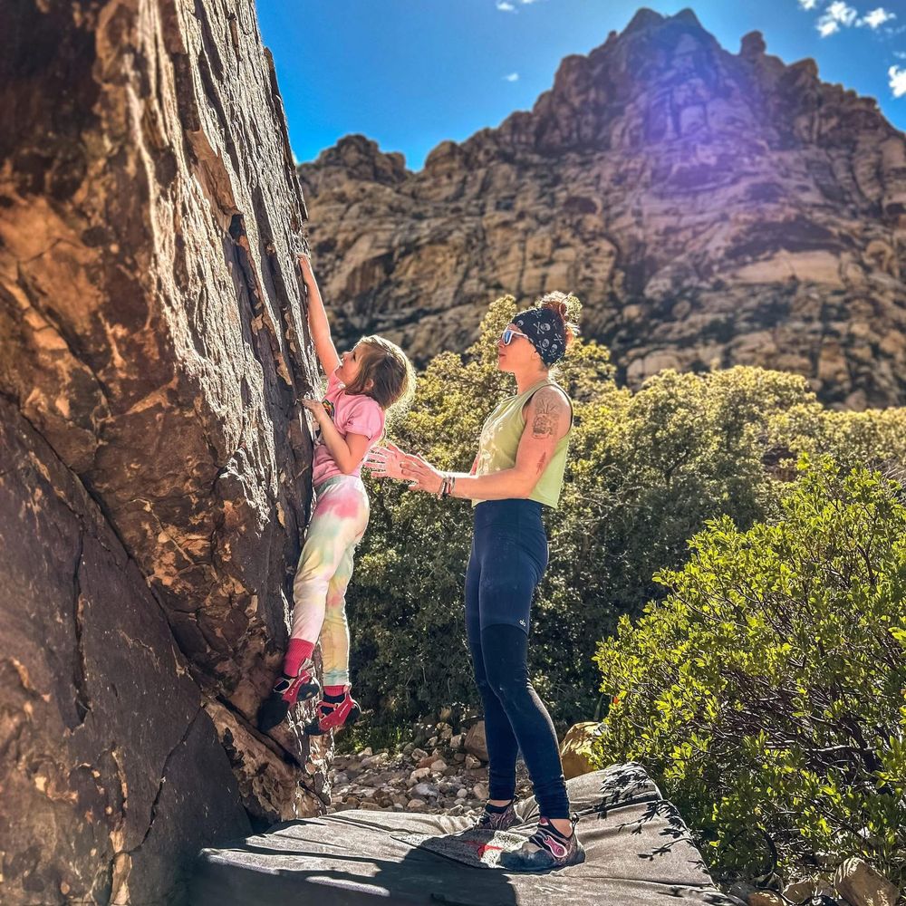 Two people practicing rock climbing techniques on sunny mountain face.