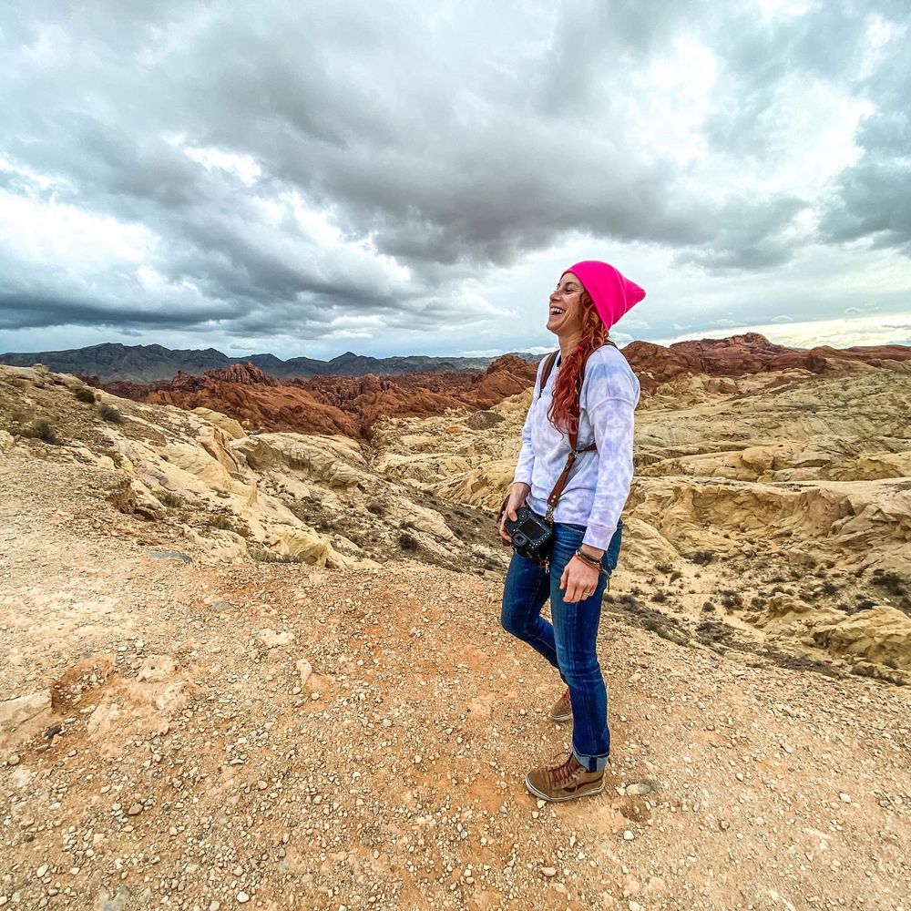 Person in pink beanie and white jacket standing on desert overlook.