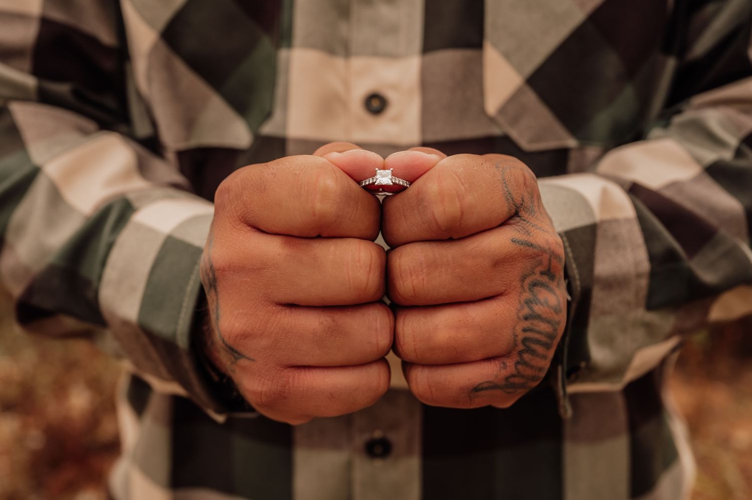 Close up of hands wearing plaid shirt showing off ring against rustic background.