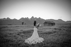 Black and white photo of a bride in a flowing dress against a mountain landscape.