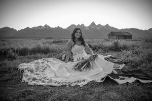 Black and white bridal portrait with mountain range and rustic cabin in background.