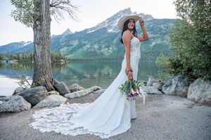 Scenic mountain lake wedding portrait with flowing white dress and natural landscape.