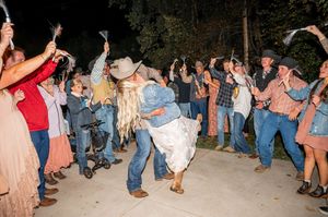 Guests dance and celebrate at an outdoor wedding reception under string lights at dusk.