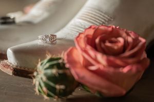 Close-up of engagement ring with coral rose and succulent on wooden surface.