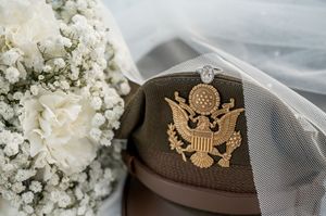 Military cap with eagle emblem next to delicate white floral bouquet arrangements.