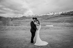 Black and white portrait of couple in wedding attire against mountainous landscape.
