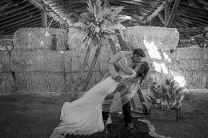 Black and white photo of romantic dip pose in front of rustic hay bale backdrop.