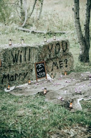 Creative marriage proposal setup with lit candles and 'Will you marry me?' written on rocks outdoors.