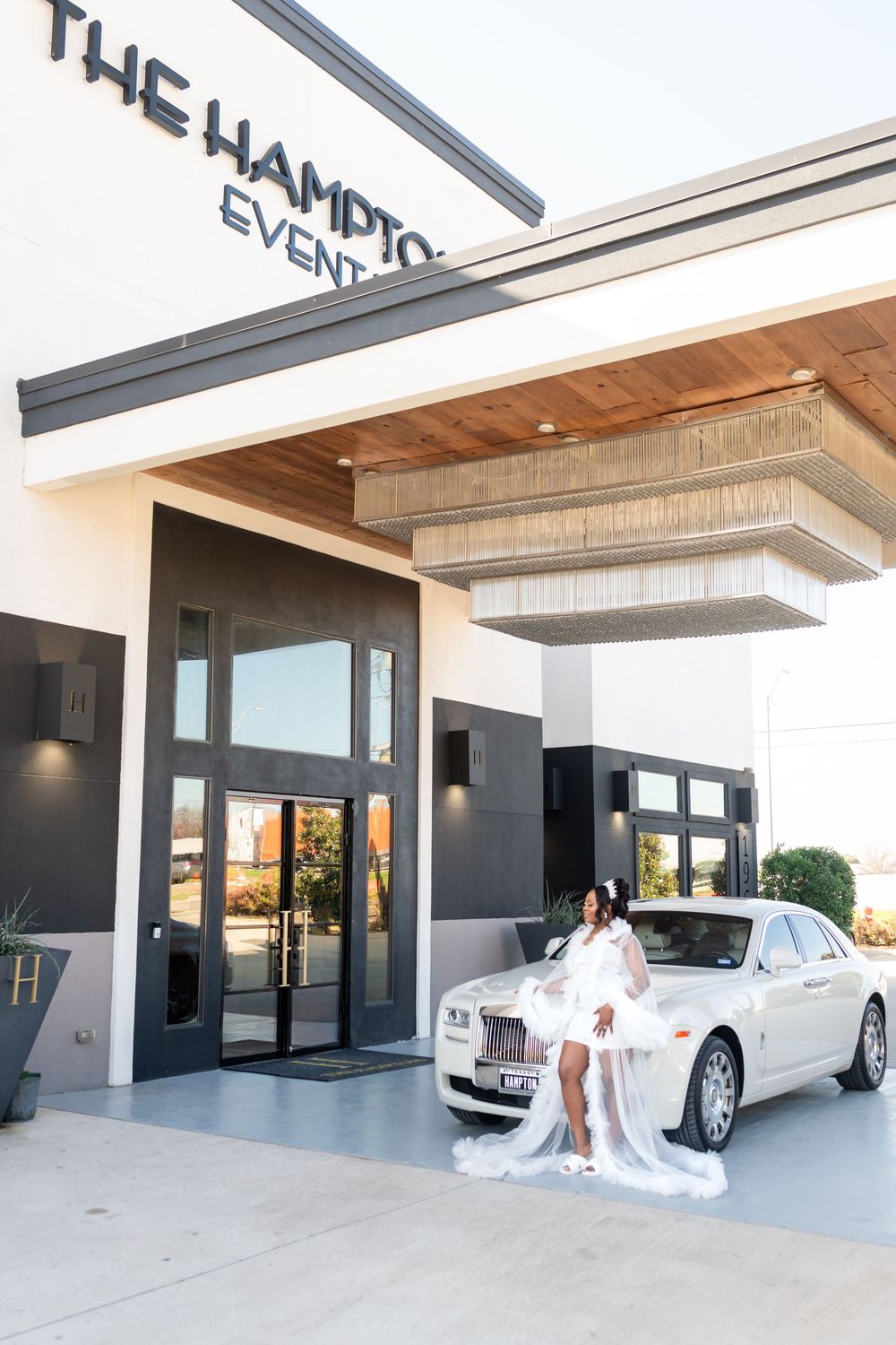 Modern white building exterior with luxury car parked under covered entrance.