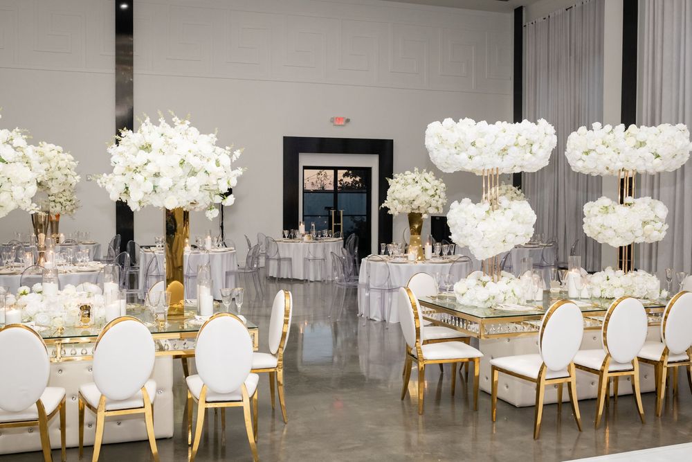 Elegant white and gold banquet chairs arranged around tables with crystal chandeliers in a modern event space.