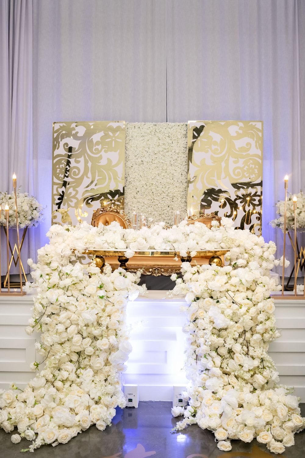 Luxurious white floral wedding display with candelabras and an ornate gold backdrop creating a romantic aisle.