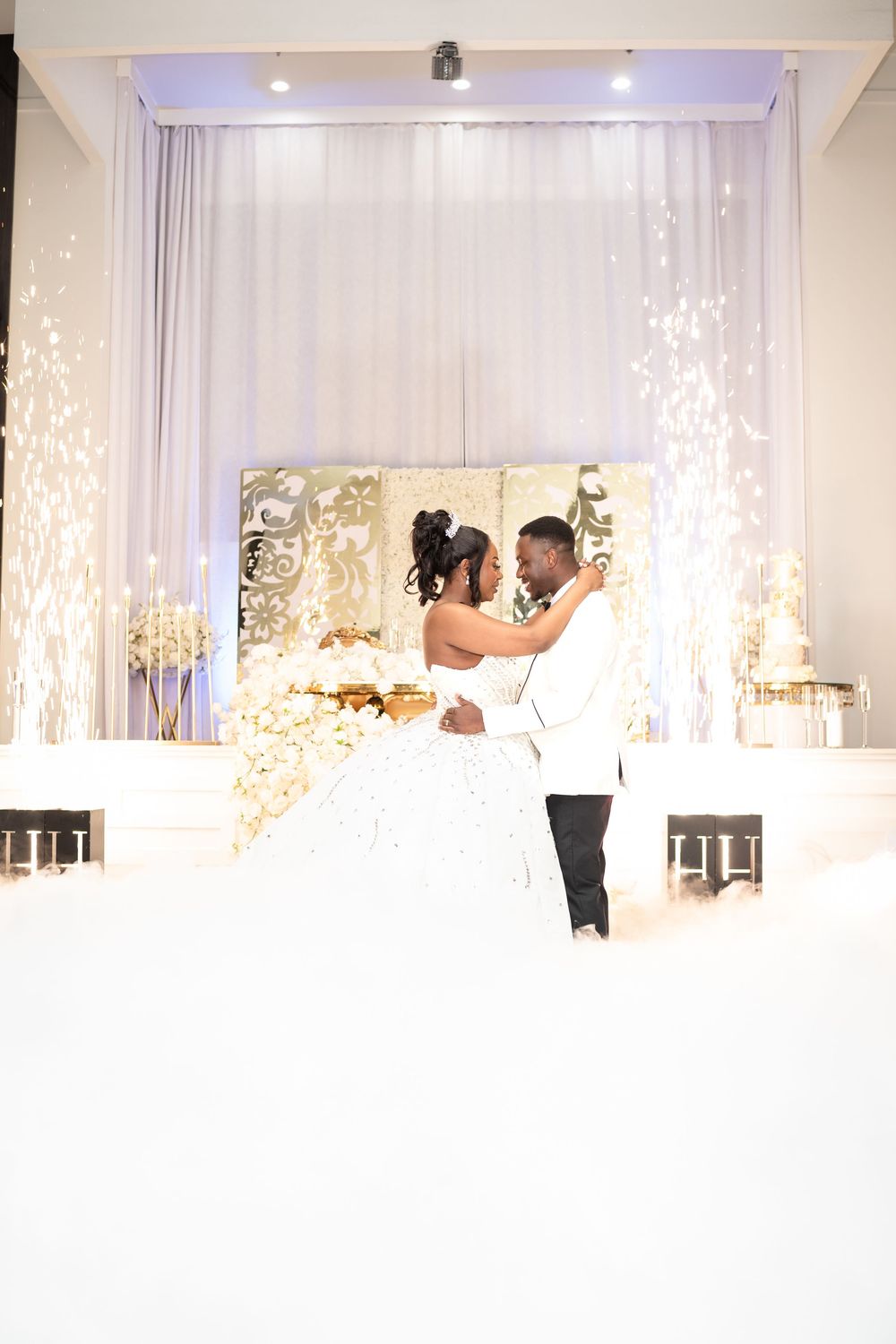 An elegant white wedding venue interior with sheer curtains and decorative lighting creating a romantic atmosphere.