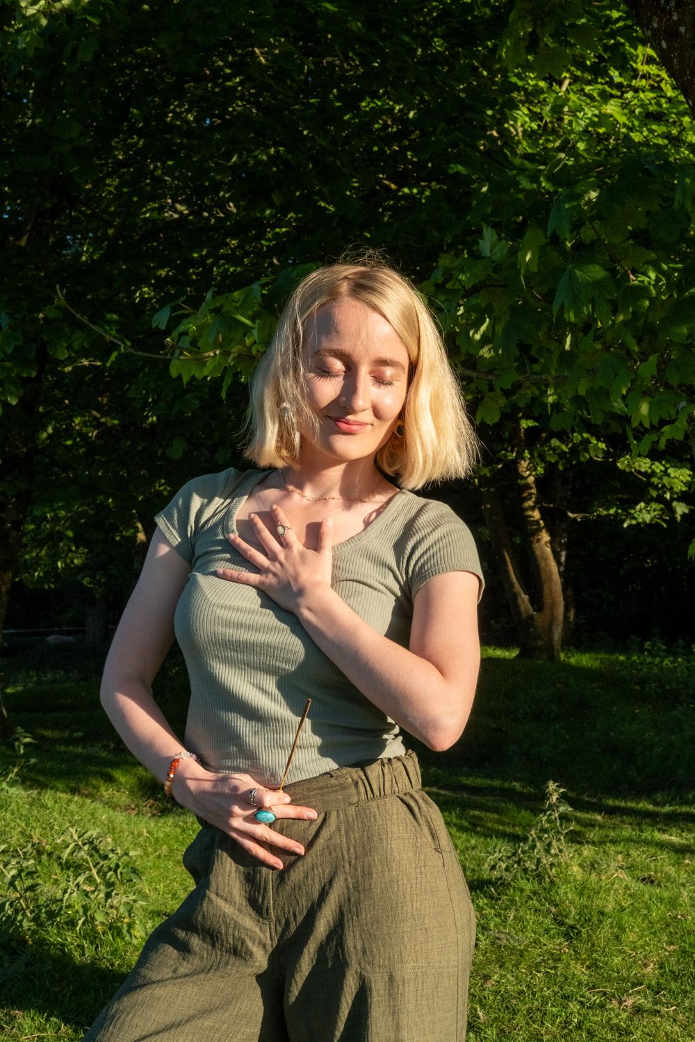 Someone in casual summer attire dances in a sunlit garden with lush green foliage in the background.