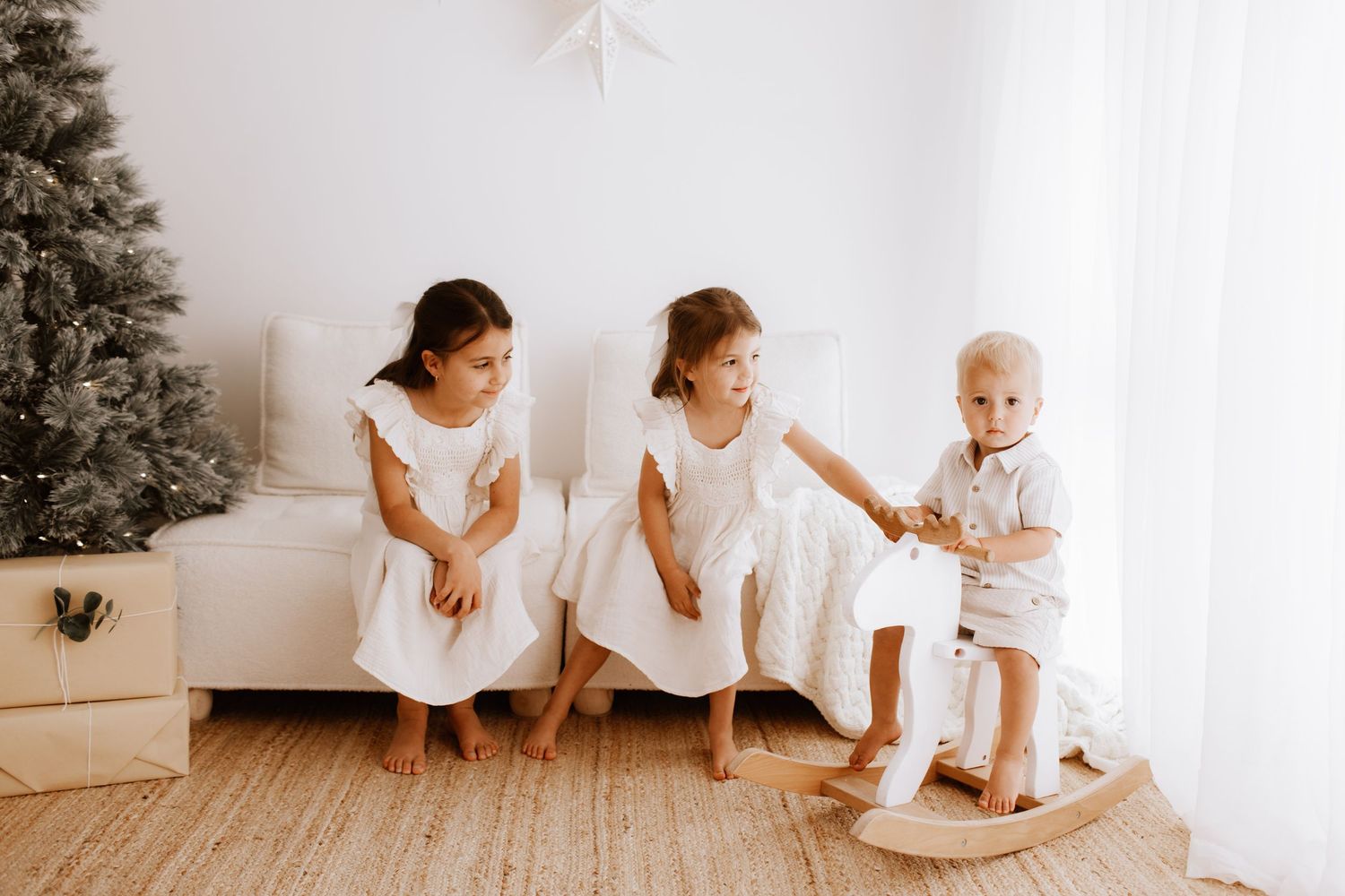 Group wearing white outfits sits together on floor near decorated Christmas tree.