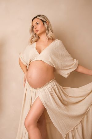 A figure in a flowing cream-coloured dress poses gracefully against a neutral beige background.