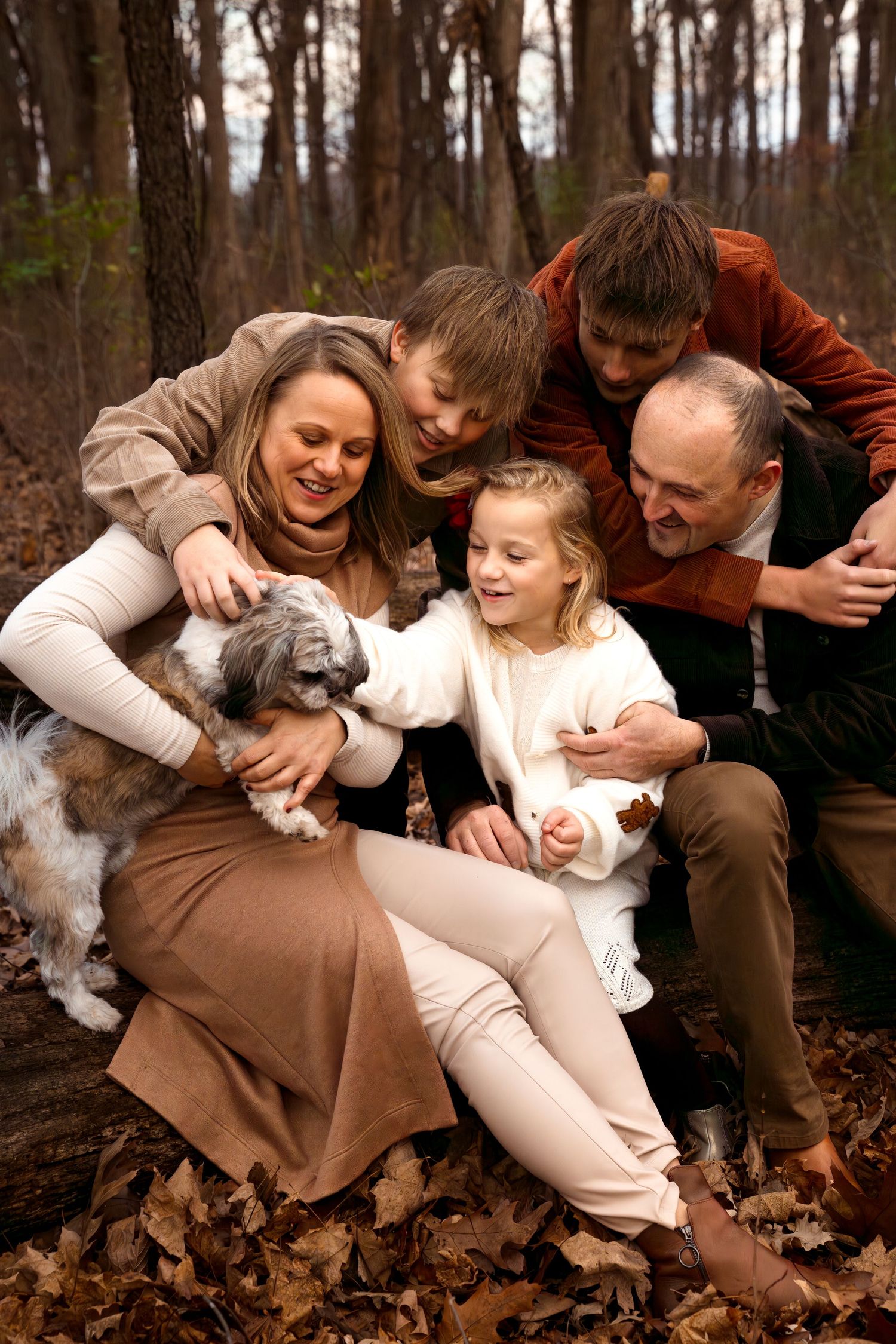 A family and their dog share a candid moment together on fallen autumn leaves in the woods.