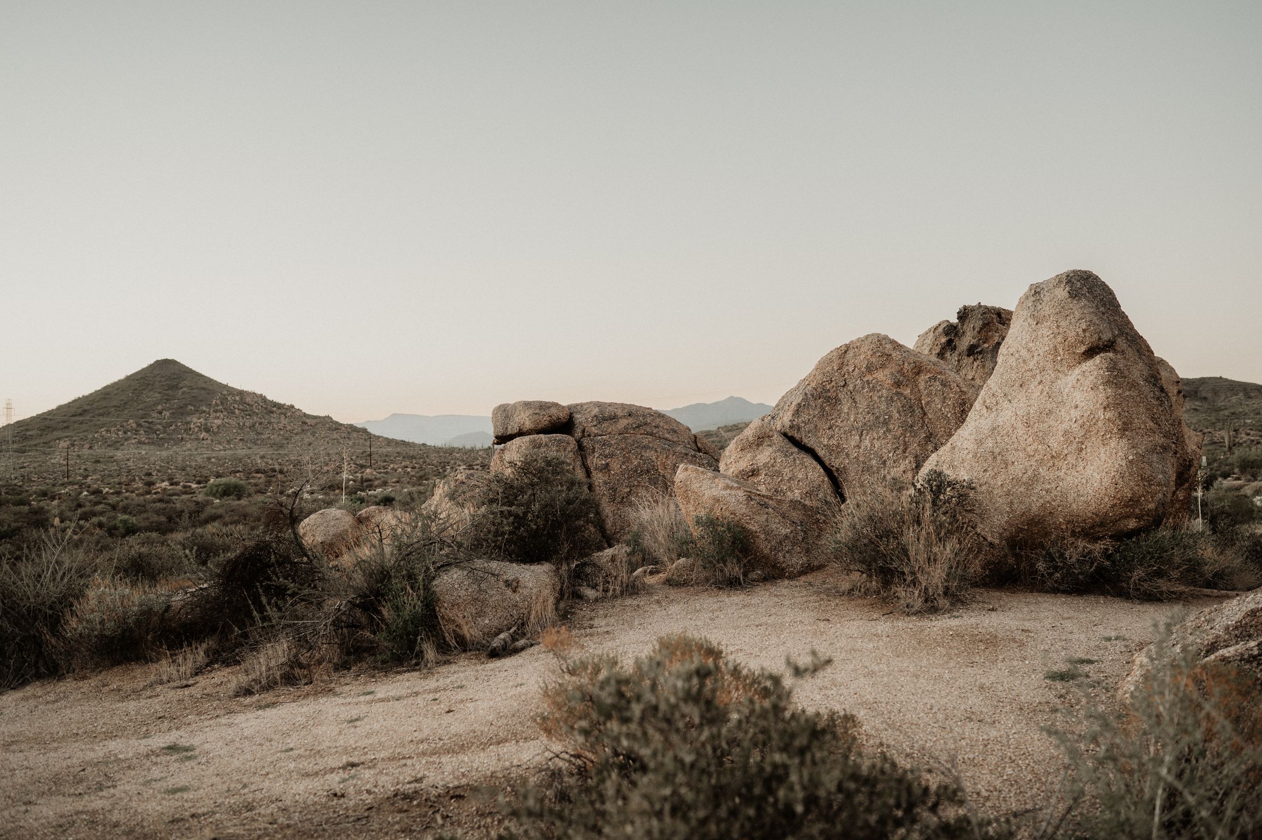 Desert landscape with scattered granite boulders and rugged mountains in the background under cloudy skies.