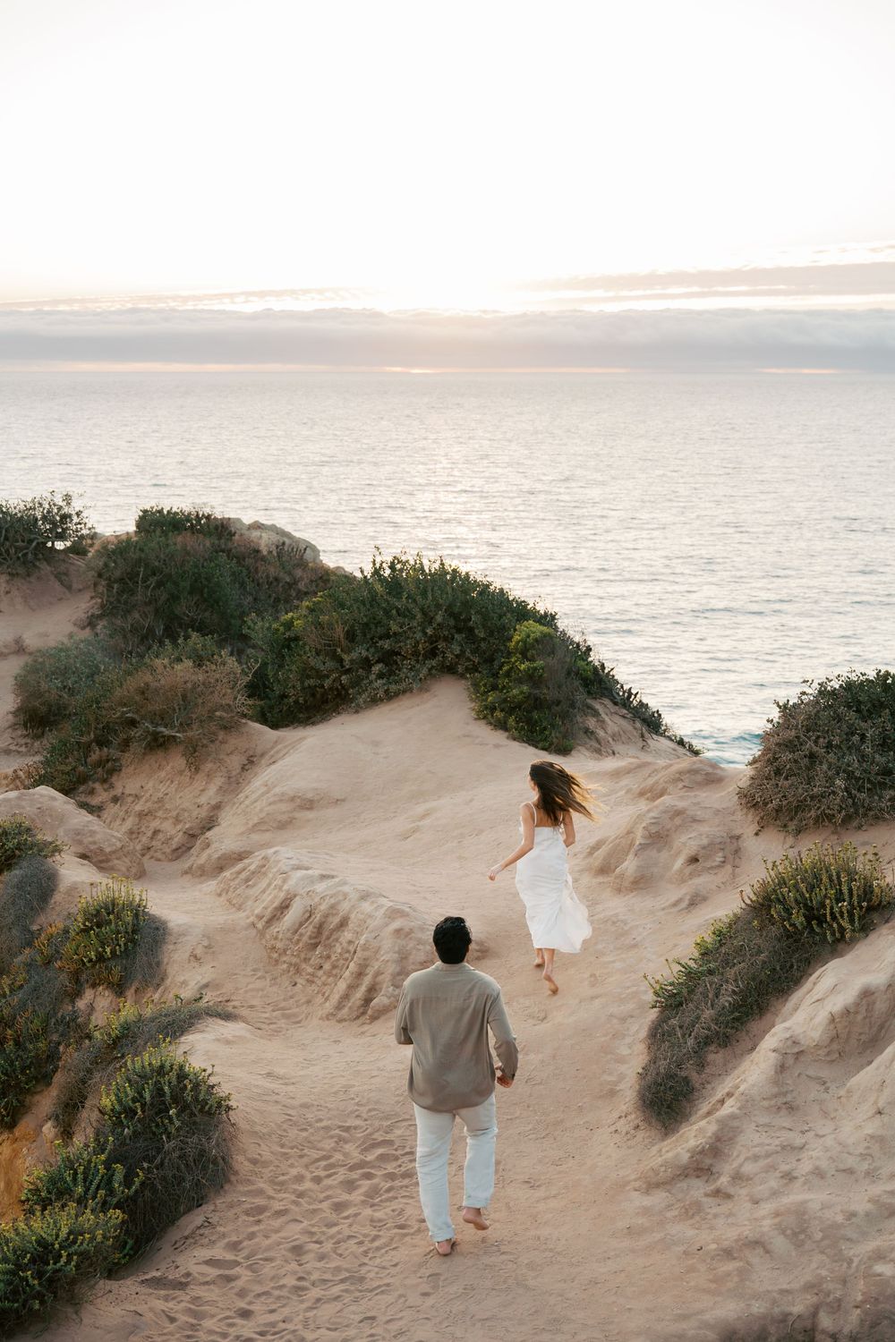 People walking along scenic coastal sand dunes at sunset overlooking the ocean.