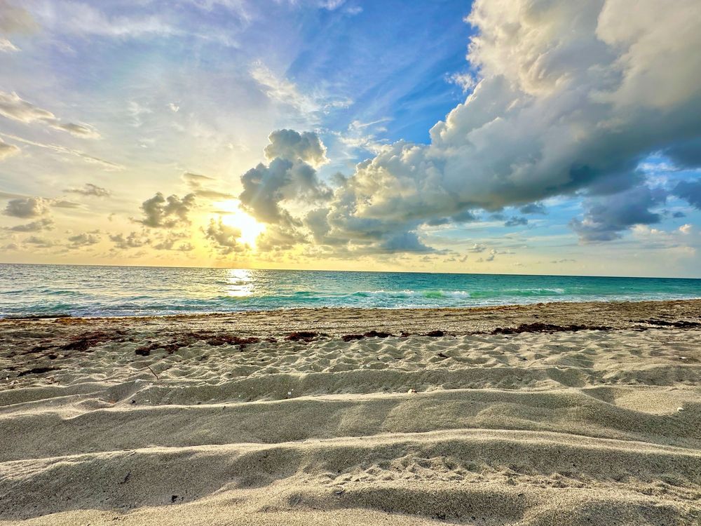 Panoramic beach scene with dramatic clouds and golden sunlight reflecting on calm waters.