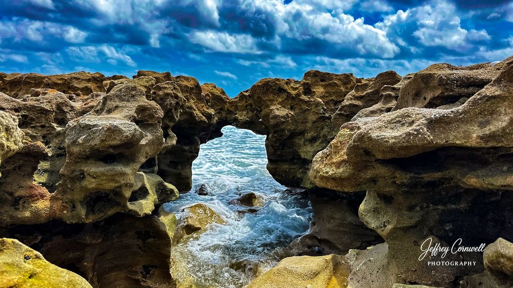 Rocky coastal formations with waves crashing against limestone cliffs under dramatic blue skies.