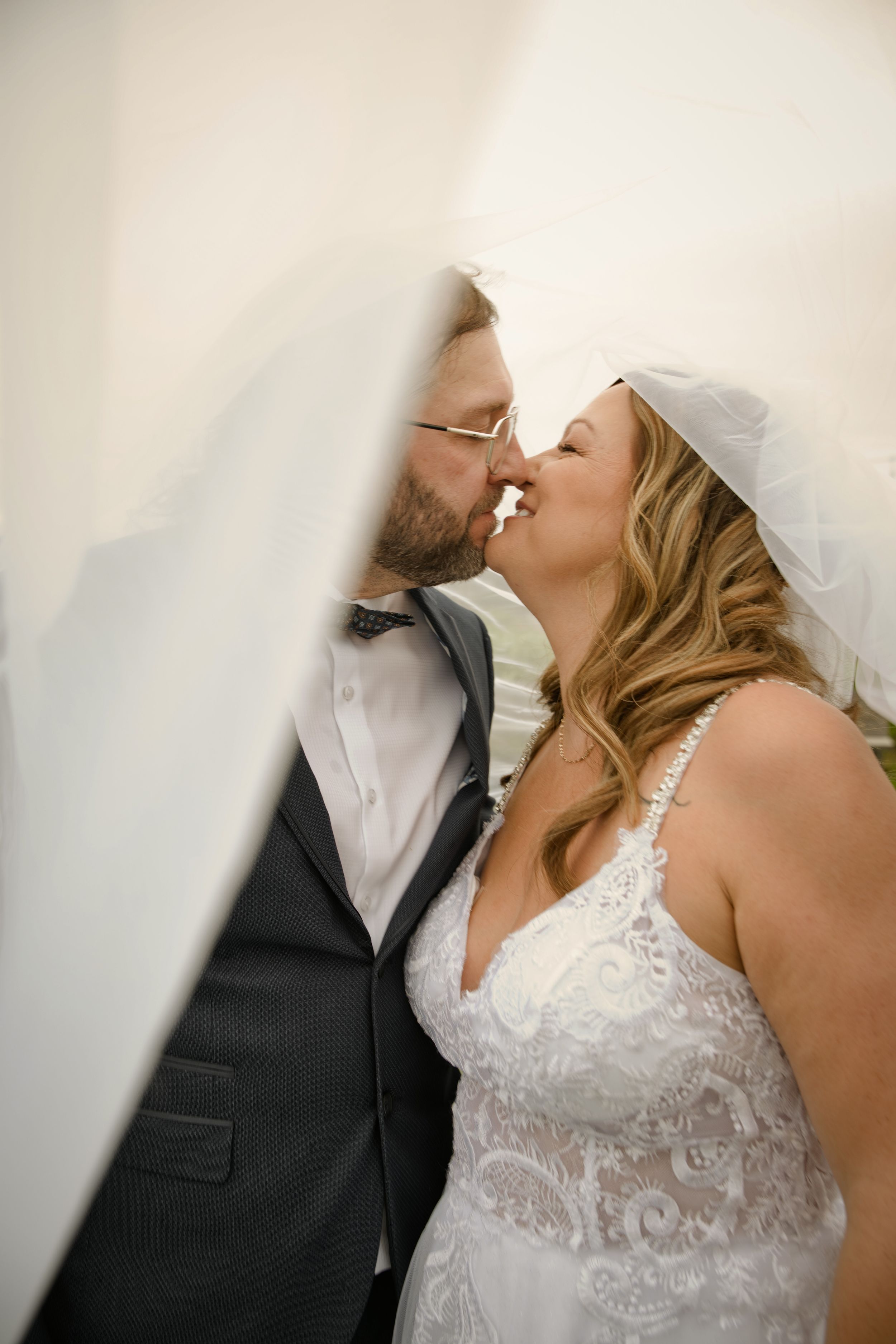 Mari et femme s’embrassant sous le voile de la mariée aux Jardins d’Alex et Jennie à Laterrière, Saguenay.