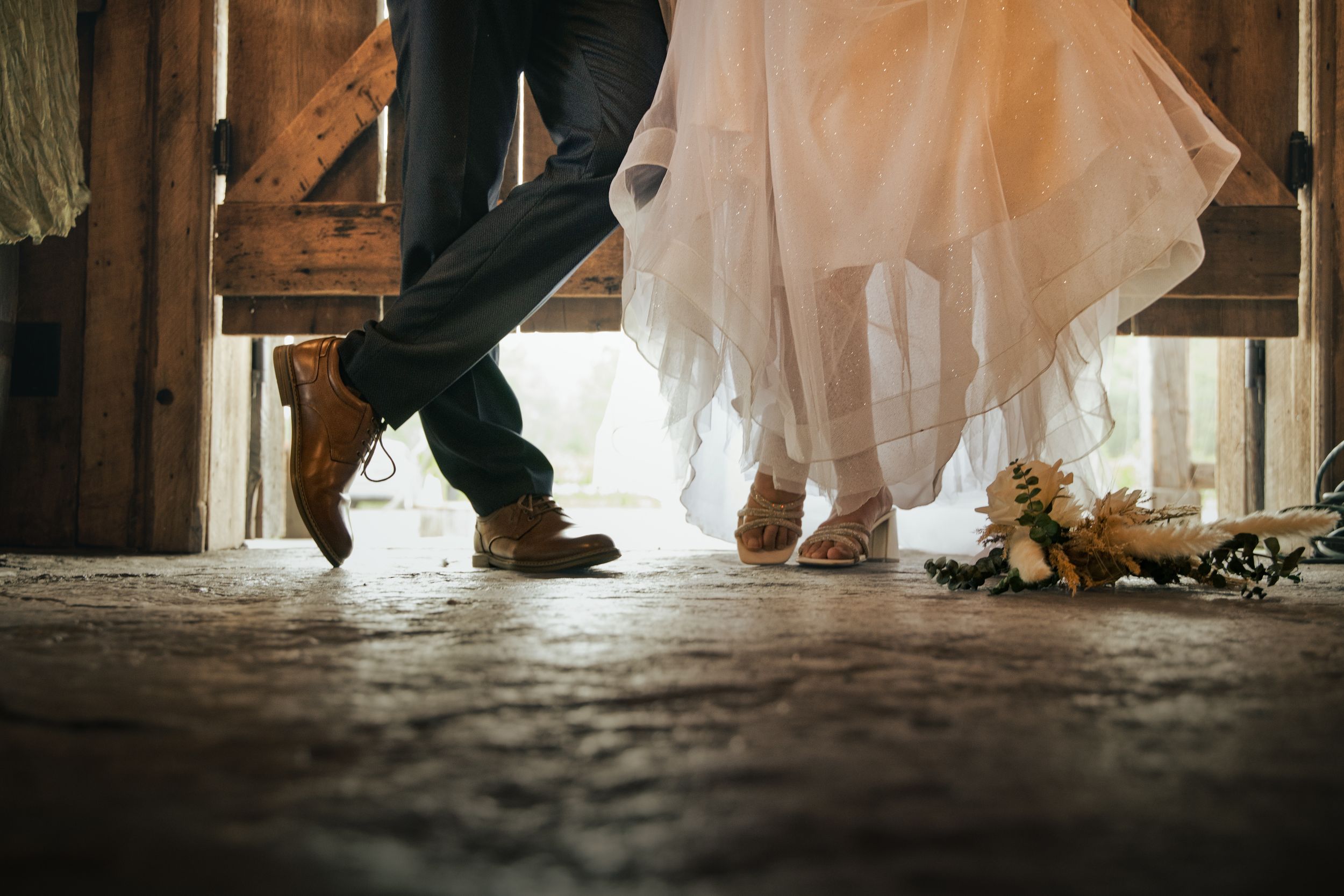 Souliers du mari, talons de la mariée et bouquet au sol dans une grange aux Jardins d’Alex et Jennie à Laterrière, Saguenay.