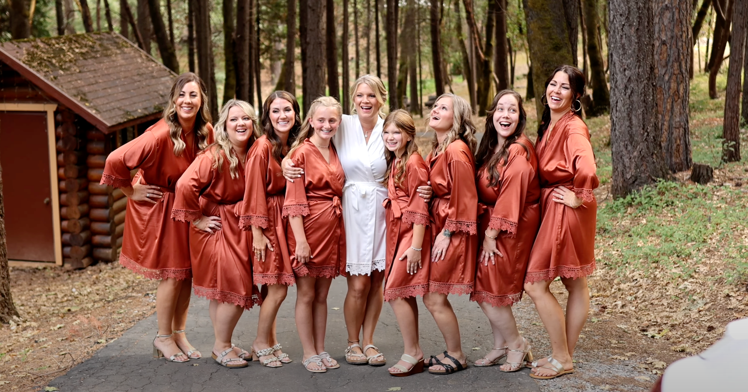 Group wearing matching rust-colored robes posing outdoors among pine trees.