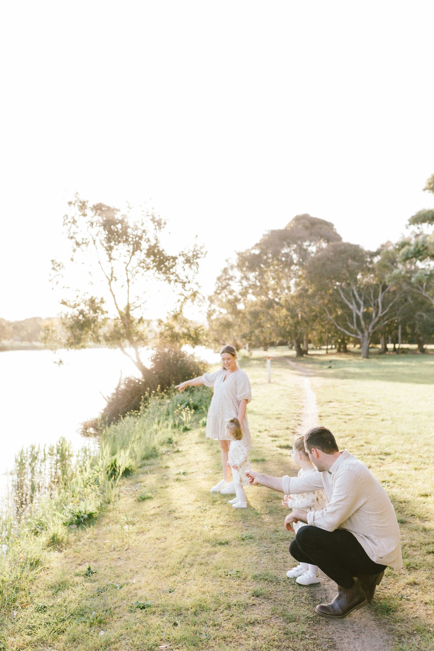 A family in white outfits plays together in a sunlit park with eucalyptus trees during sunset.