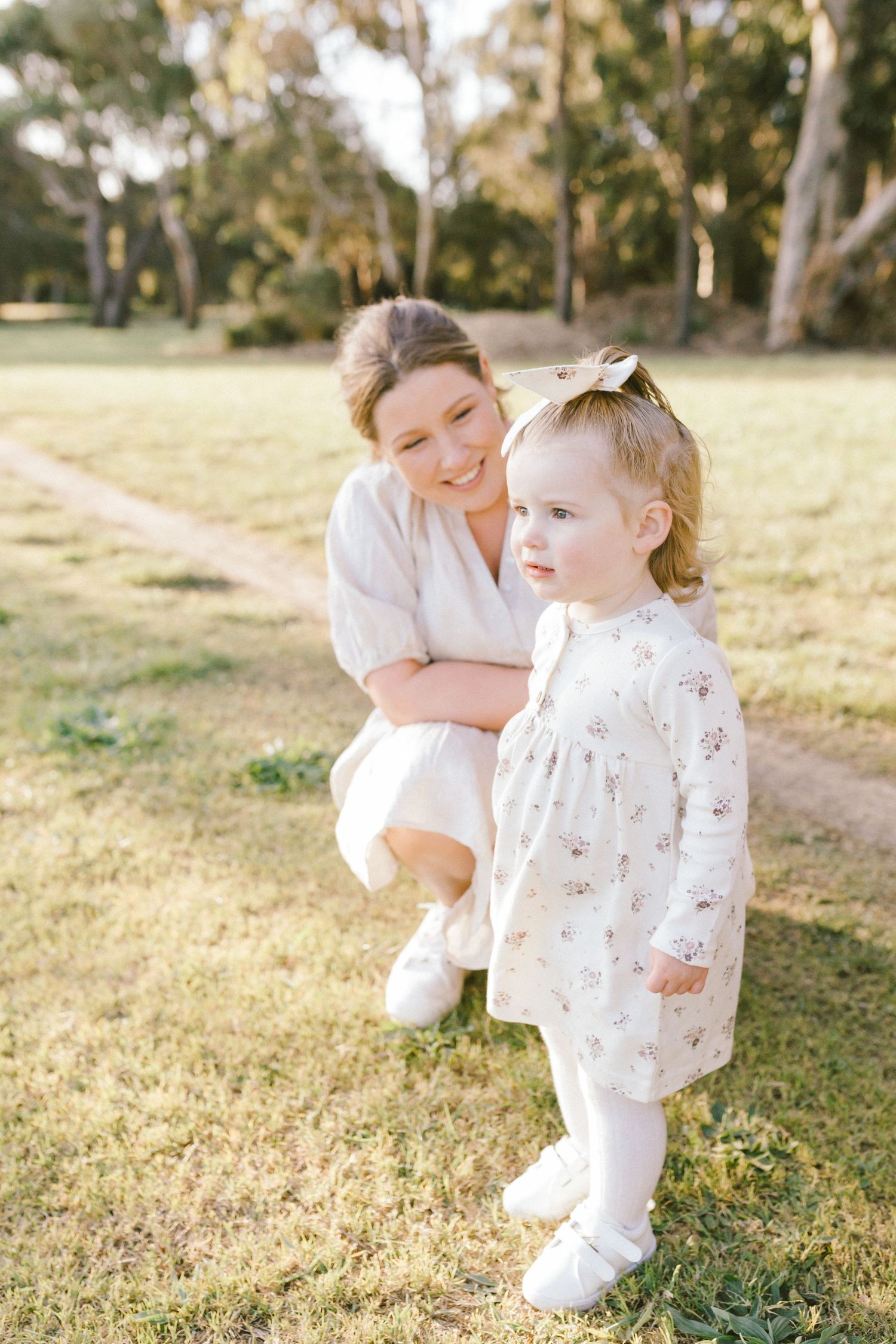 Family in white outfits playing together in a grassy field during golden hour sunset.