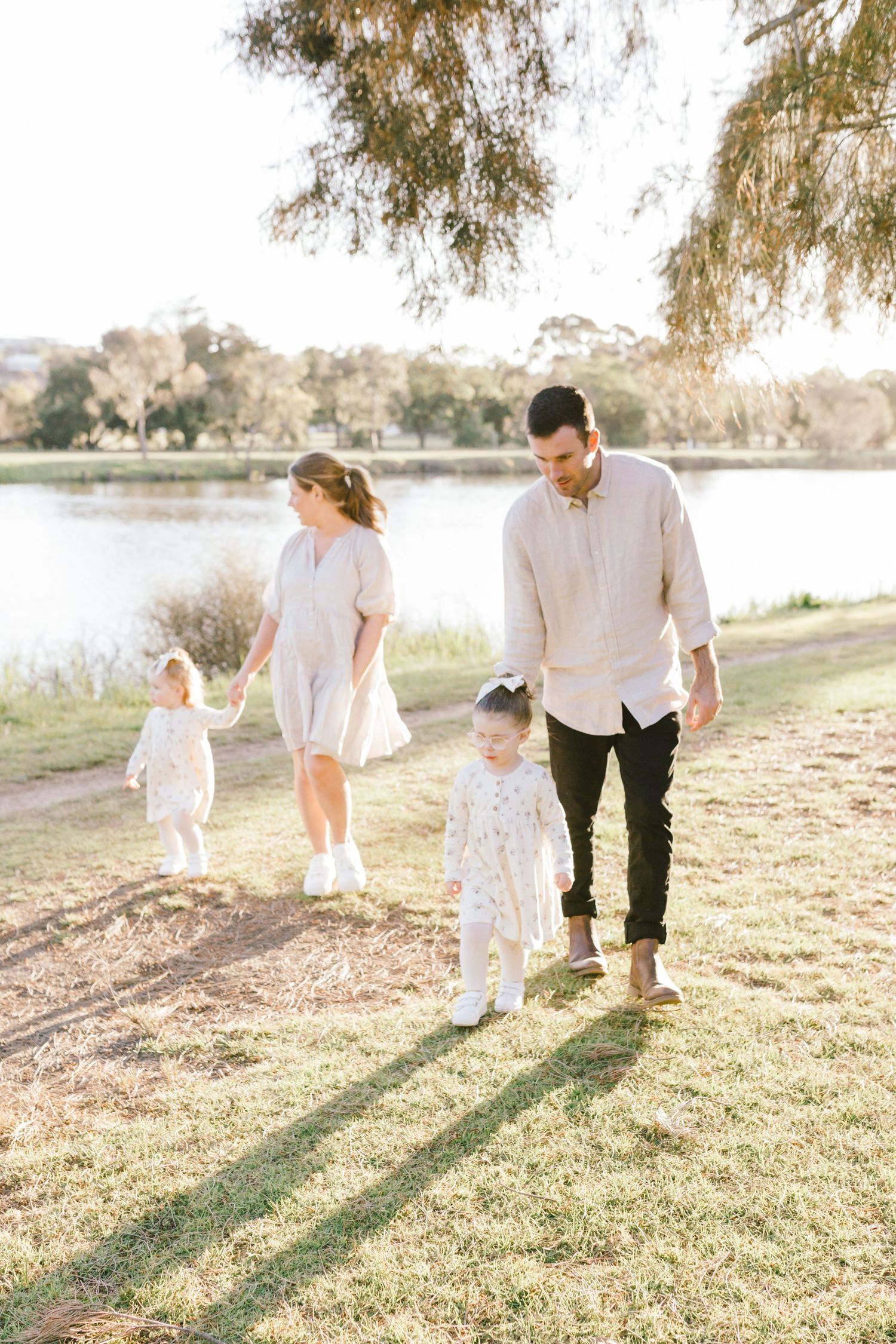 A family taking a sunset stroll along a grassy lakeside path casting long shadows on a warm evening.