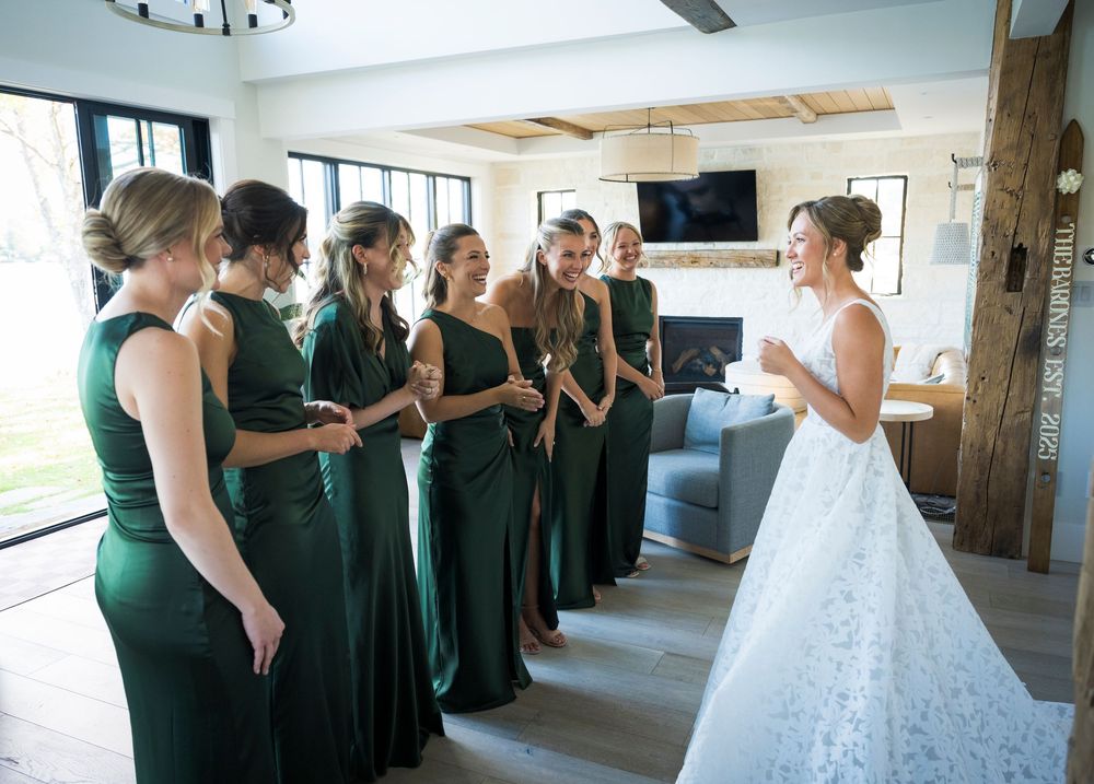 Bridesmaids in emerald green dresses gather around the bride in a white lace gown.