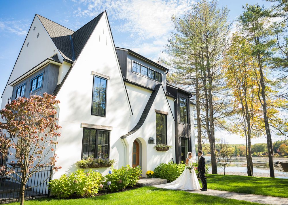 An elegant white modern house with black trim and tall windows overlooking a waterfront.