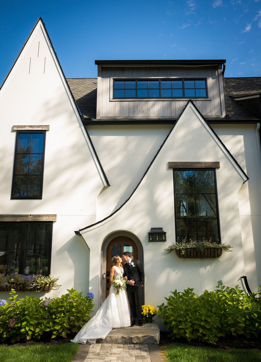 A modern white Tudor-style house with a curved entrance and window boxes filled with flowers.