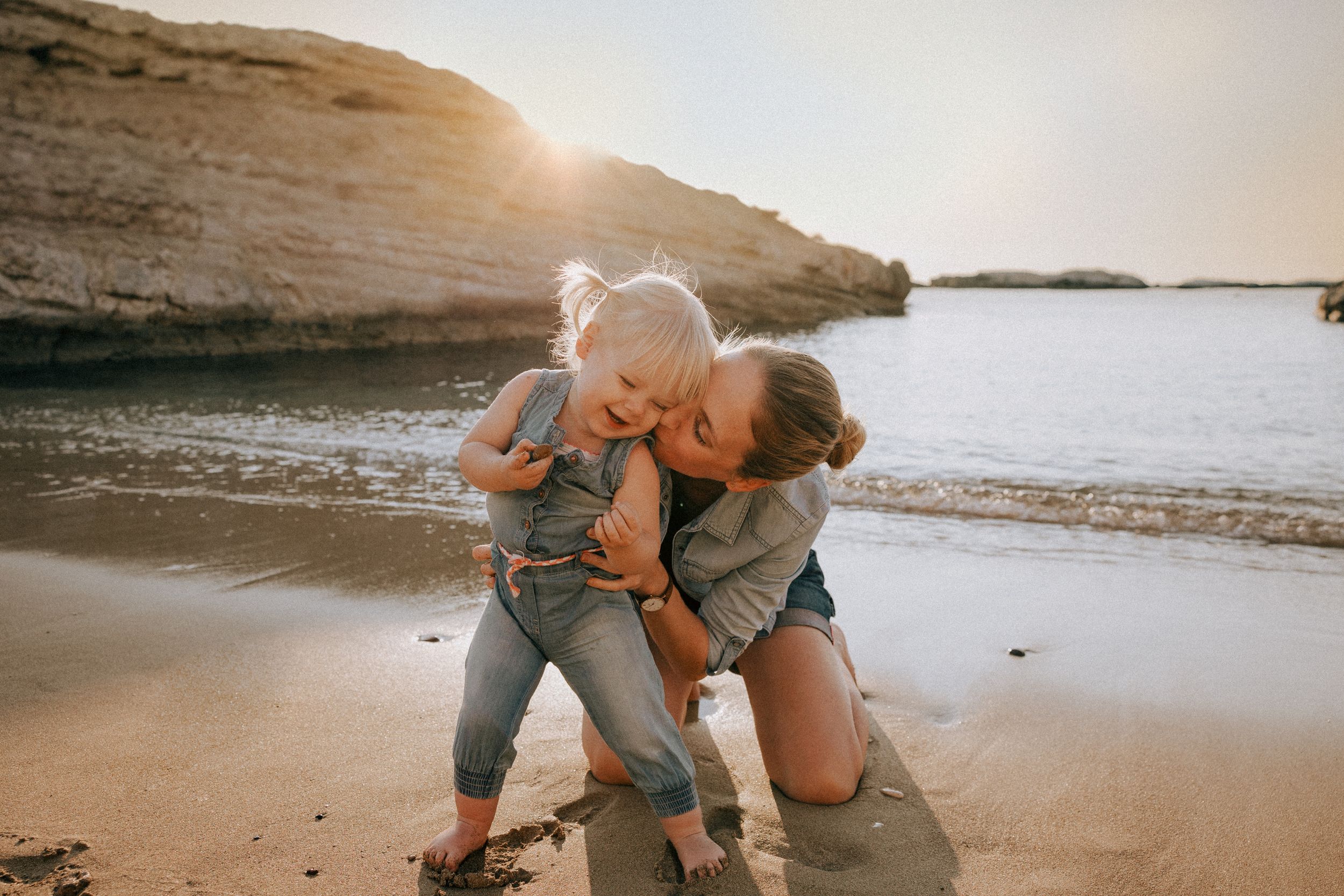 Family embracing and playing on a scenic beach at sunset with rocky cliffs in the background. Paphos family photographer