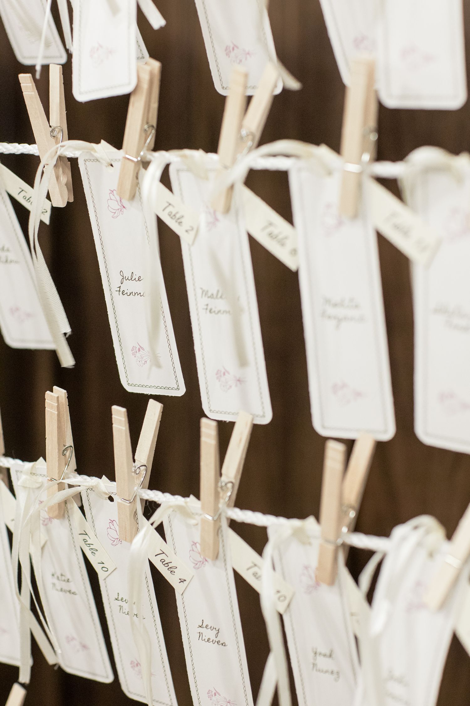 White name cards attached to a wall with small clothes pins create an elegant seating chart display for an event.