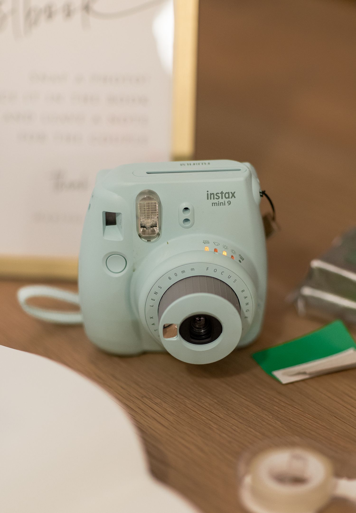 A mint green Fujifilm Instax Mini instant camera sits on a wooden surface next to office supplies.