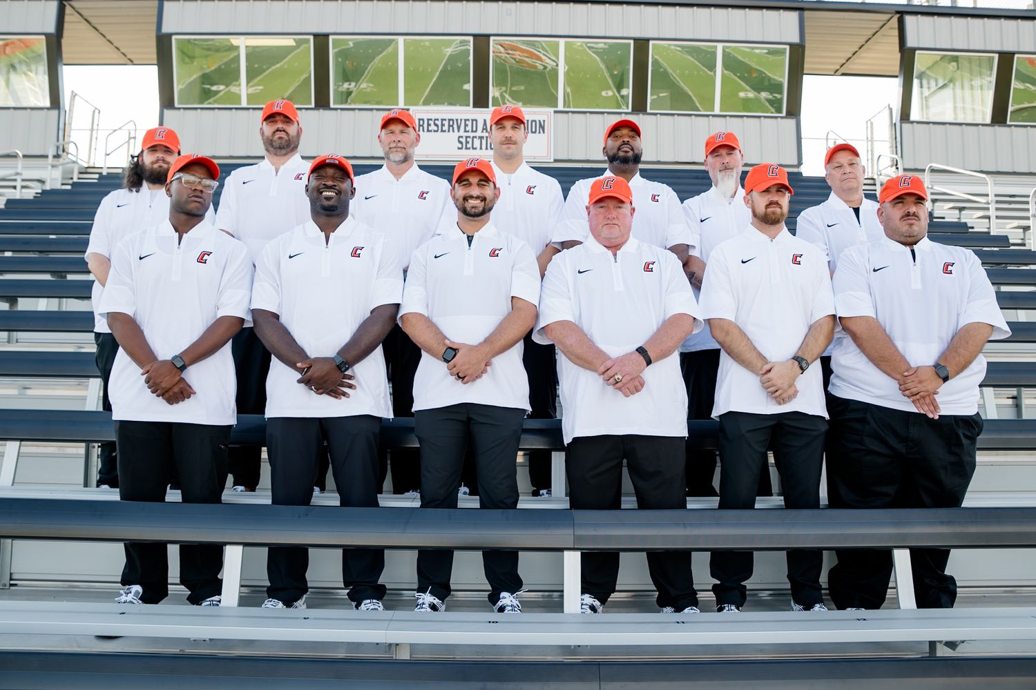 A group of chefs in white uniforms and red caps stand together in rows on stadium bleachers for a formal team photo.