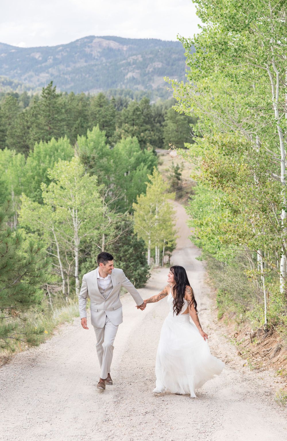 A couple walks playfully down a mountain path lined with aspen trees on their wedding day.