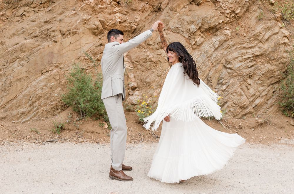 Playful moment of couple dancing on a dirt path with rocky cliff behind them.