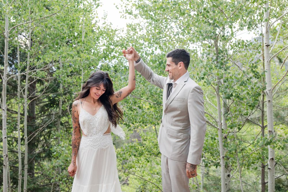 A couple in light colored wedding attire dancing together among aspen trees.