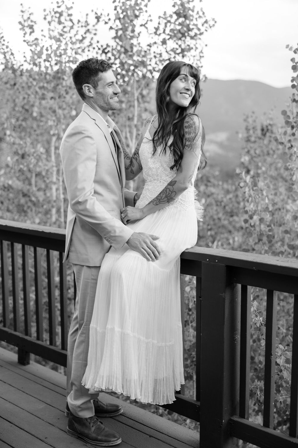 Newlyweds share a joyful moment on a wooden deck with mountain views in the background.