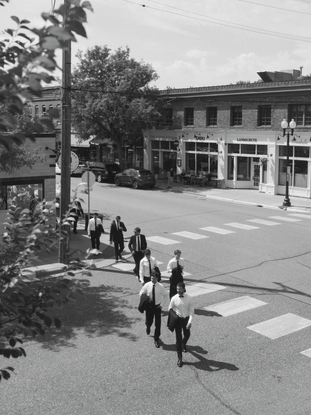 Wedding guests walk in progression across a paved sidewalk in front of a commercial building.