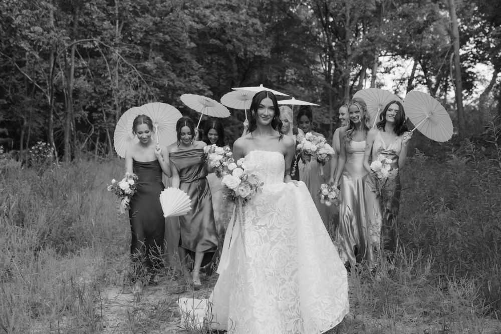 A group poses with decorative parasols in a natural outdoor setting with tall grass and trees.