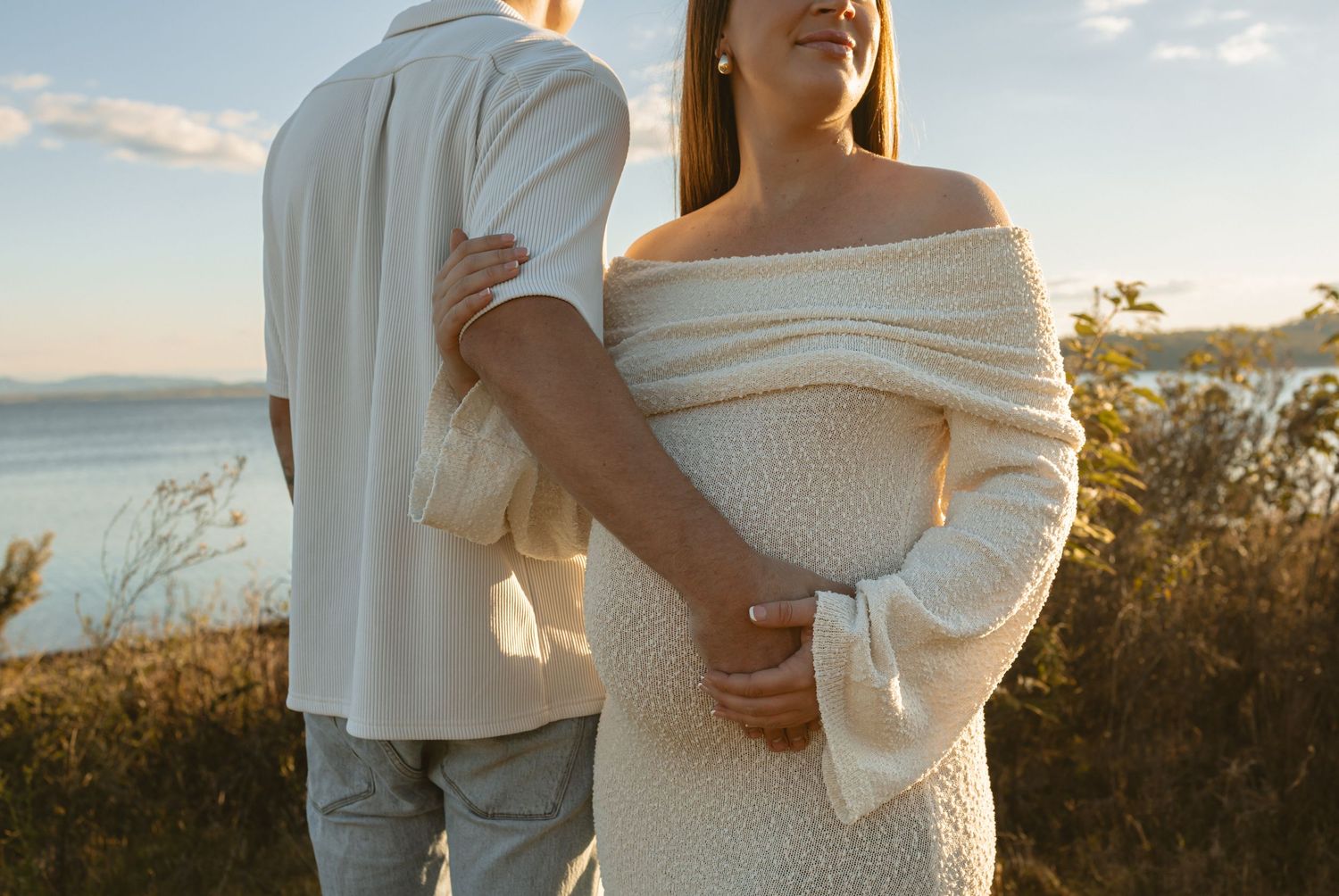 A romantic coastal photoshoot at sunset with two people in flowing white attire posing among natural scenery.