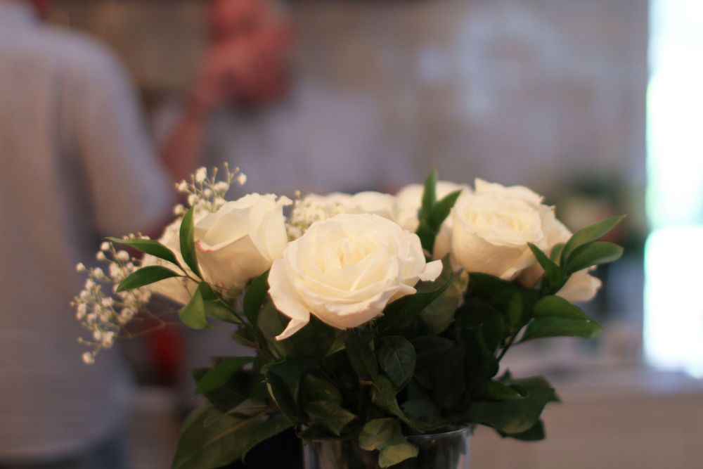 White roses and greenery in clear vases arranged along a decorative shelf with wedding styling elements.