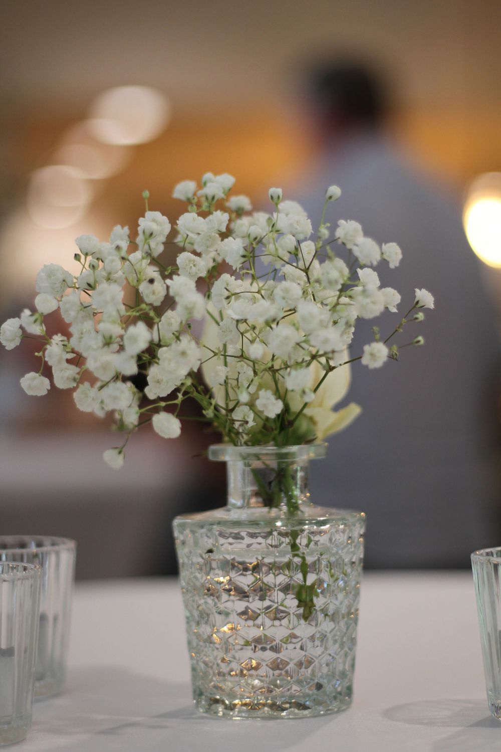 Delicate baby's breath flowers arranged in a textured glass vase on a white tablecloth.