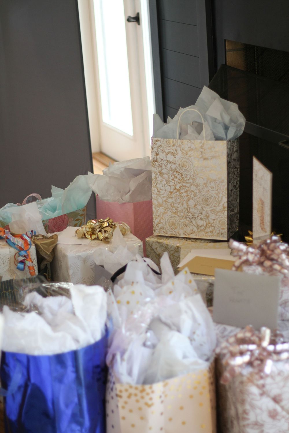 Collection of wrapped presents and gift bags in blue and white tones arranged near a window.