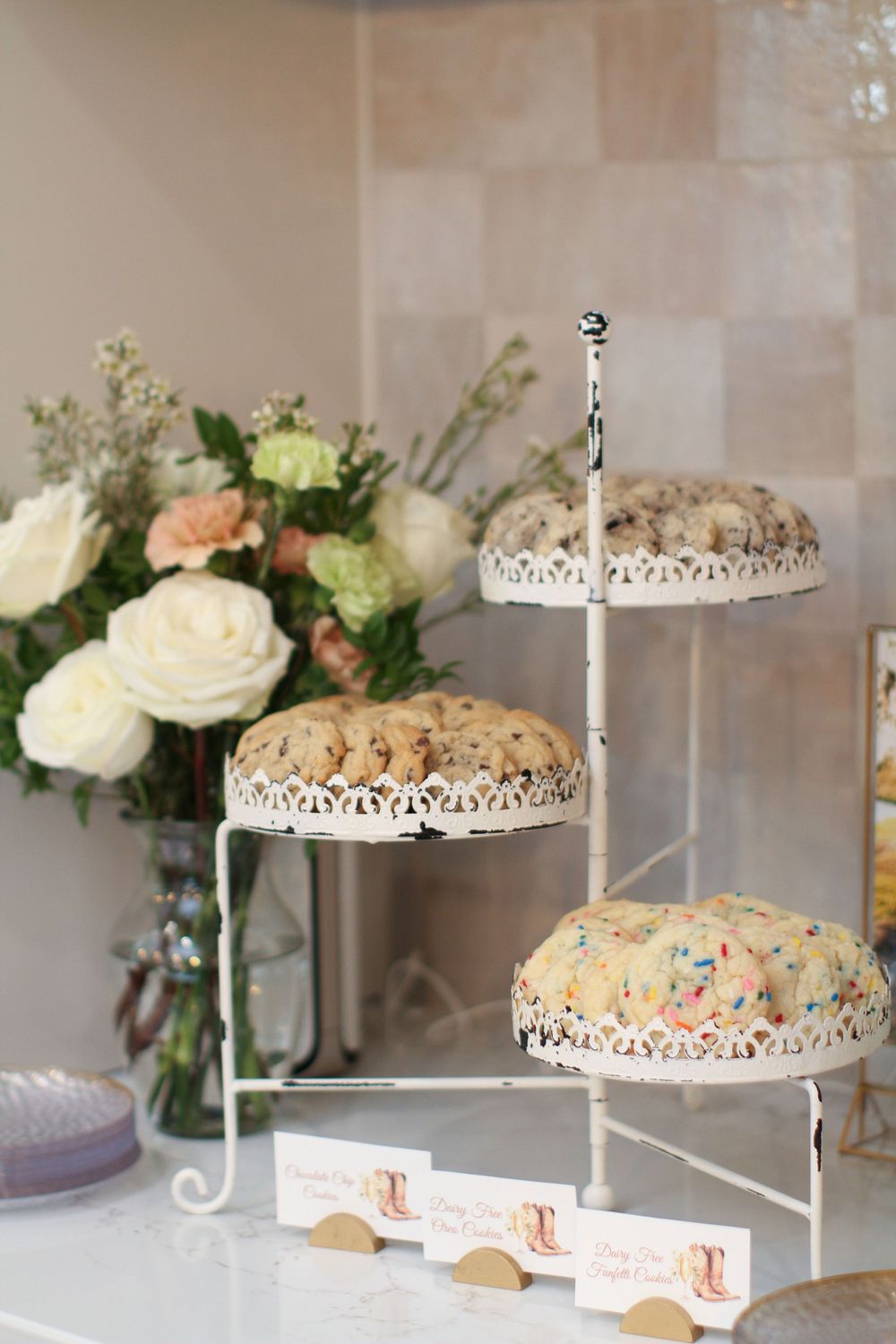 Wedding dessert display featuring ornate white cake stands with delicate lace-like details and fresh floral decorations.