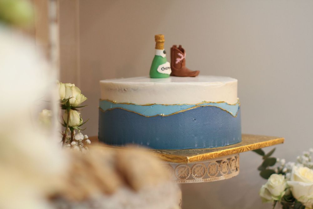 A blue and white wedding cake decorated with gold leaf and white floral accents sits elegantly on a marble surface.