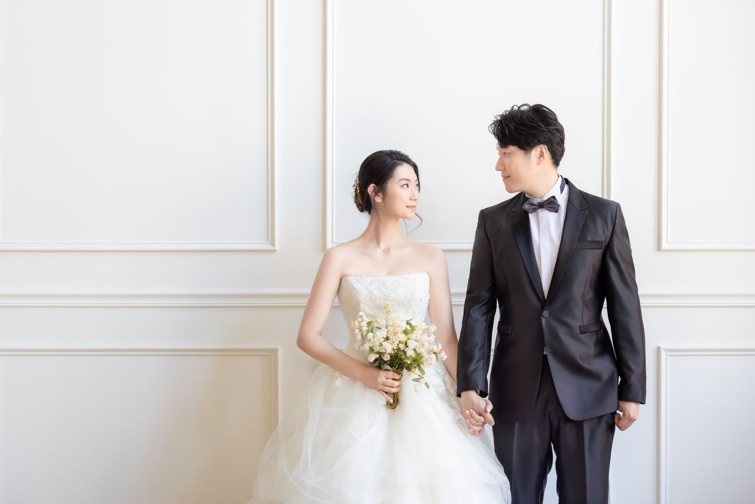 A couple shares a tender moment in a bright white studio with elegant molding details on the walls.